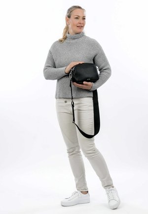Borsa a tracolla in pelle nera con finitura texturizzata, hardware in argento e tracolla removibile, tenuta da una persona che indossa un maglione grigio.