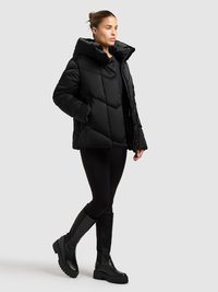 Schwarze Steppjacke mit hohem Kragen, Rautenmuster und Frontreißverschluss. Kombiniert mit schwarzen Leggings und kniehohen Plateaustiefeln.