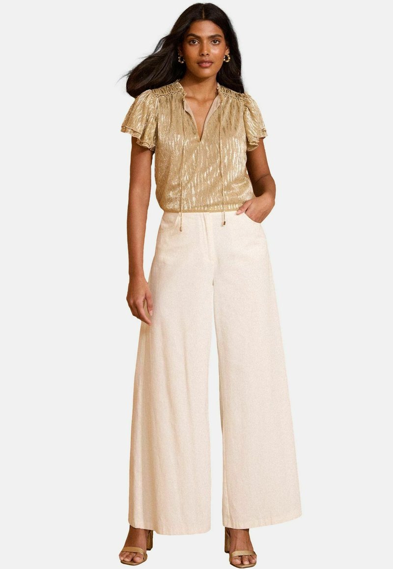 Gold metallic short-sleeve top with a drawstring neckline paired with cream wide-leg trousers, featuring side pockets and a textured fabric.