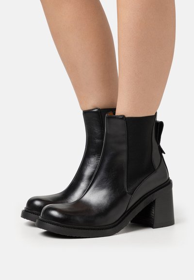 Botas de tobillo de cuero negro con punta redondeada, paneles laterales elásticos y un tacón grueso. Textura lisa con un pequeño detalle de tira en la parte trasera.