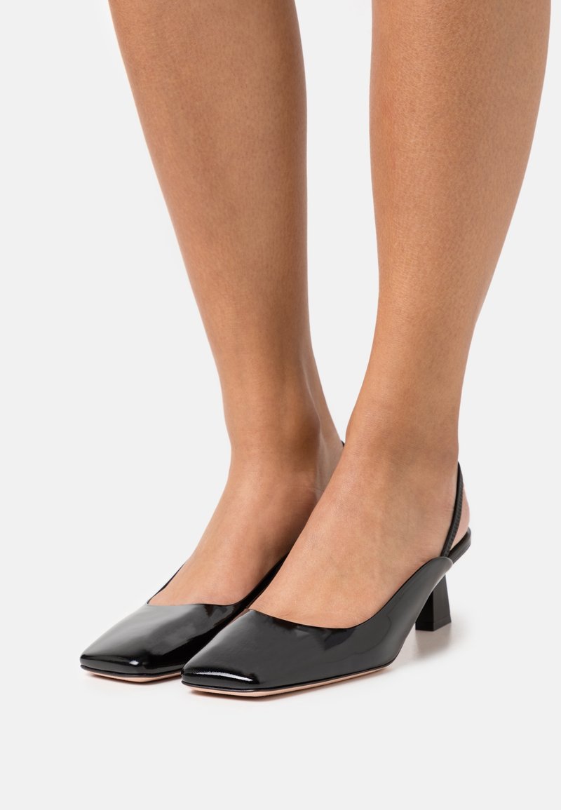 Talons hauts effet patent noir avec bride arrière, bout carré et talon block, présentant une texture lisse et un design minimaliste.