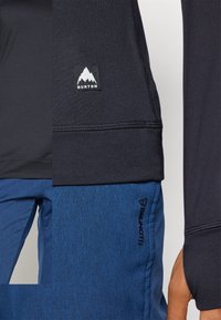 Black long-sleeve athletic top with a logo patch and blue textured pants featuring side branding and contrasting seams.