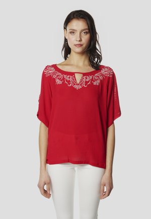 Blusa roja con escote en forma de ojo de cerradura, bordado floral blanco en el cuello y mangas cortas y anchas. La tela es ligera y texturizada.