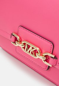 Sac à main en cuir rose avec fermoir chaîne dorée portant le logo "MK". Texture lisse avec surpiqûres contrastées. Forme rectangulaire, design moderne.