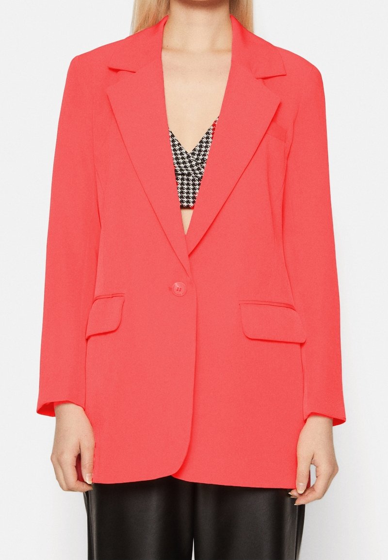 Blazer rosa corallo realizzato in tessuto morbido, con colletto a pistagna, chiusura con un bottone e due tasche frontali.