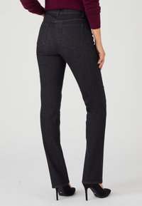 Jeans de mezclilla negra con corte recto, bolsillos traseros y una cintura de altura media, combinados con unos zapatos de tacón alto negros.
