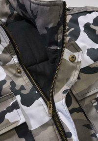 Chaqueta de camuflaje con una mezcla de verdes oscuros, grises y blancos. Cuenta con un zipper dorado, dos bolsillos frontales y un forro interior acolchado.