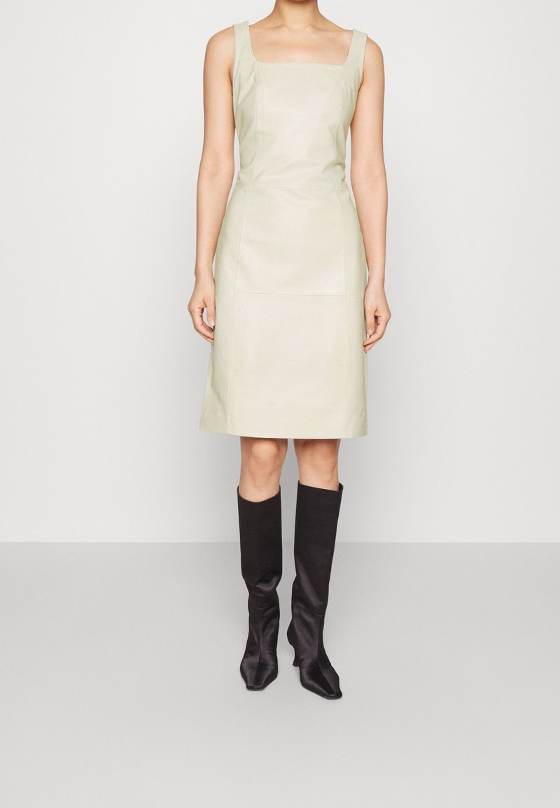 Robe à manches courtes, décolleté carré en cuir vert clair, corsage ajusté et jupe à la longueur du genou, associée à des bottes en tissu noires montantes.