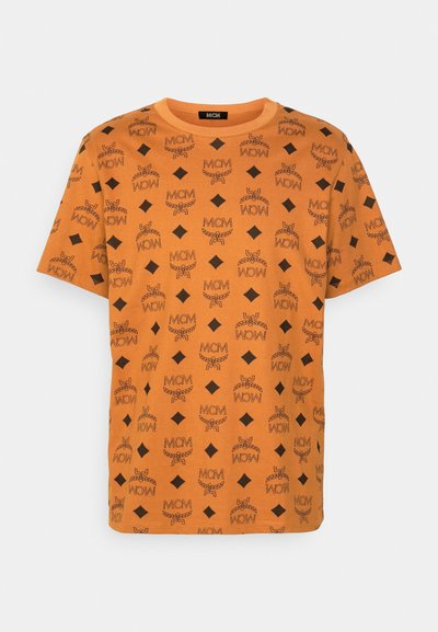 Orange bomull t-shirt med ett upprepat svart grafiskt mönster med "MCM" text, diamantformer och kedjemotiv. Crew neck-design.