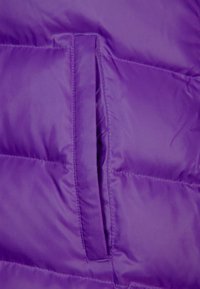 Tissu de veste matelassée violet avec une texture lisse. Comprend une poche zippée située au centre de l'avant pour le rangement.