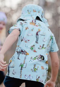 Kortärmad, ljusblå skjorta med fantasifulla mönster av djur och människor som är engagerade i olika aktiviteter, tillverkad av bomullstyg.