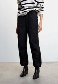 Pantalons cargo noirs avec une coupe décontractée, taille élastique et poches latérales. Associé à un pull à rayures noir et blanc et des bottines.