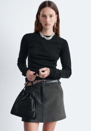 Black long-sleeve top with ribbed cuffs, gray tweed skirt with pockets, and small black drawstring bag. Silver chain necklace and ring accents.