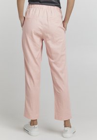 Lys rosa bukser i linblanding med elastisk midje, som har to baklommer og en avslappet passform, som smalner noe inn ved anklene.