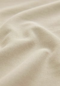 Vaalea beige teksturoitu kangas hienovaraisella ruudullisella kuviolla, jossa pehmeät, sileät laskokset ja kevyt, ilmava ulkonäkö.