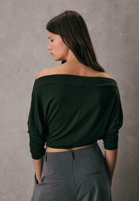 Čierny crop top s odhalenými ramenami vyrobený z mäkkej látky s dlhými rukávmi, kombinovaný so šedými strihanými nohavicami s vrecom na zadnej strane a hladkým povrchom.
