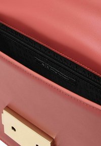 Interno di una borsa a tracolla in pelle rosa con hardware dorato, fodera nera caratterizzata da un motivo con logo e tasca con zip per una conservazione sicura.