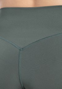 Leggings de tiro alto en color verde oscuro, fabricados con un tejido suave y un diseño sin costuras, con detalles de costura sutiles en la parte posterior.
