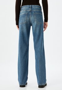 Jeans de mezclilla azul de talle alto con un corte relajado, que presentan dos bolsillos traseros y una cremallera. La tela tiene un acabado suave y texturizado.