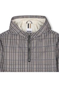 Gobtu džemperis su gaubtu, pagamintas iš zigzago rašto audinio, turi priekinį užtrauktuką, juodos spalvos apdailą ir smėlio bei kreminės spalvos vidinį pamušalą. Matomas prekės ženklo ženklinimas.