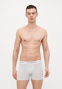 Hvide bomuldsboxere med en sort logoelastic, tætsiddende design og glat tekstur. Modellen står oprejst mod en ensfarvet baggrund.