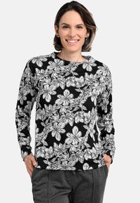 Floral long-sleeve top in black with white floral pattern. Round neckline, soft fabric, fitted cuffs, and relaxed fit. Paired with gray pants.