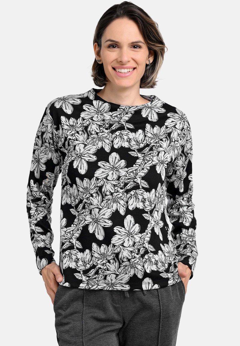 Floral long-sleeve top in black with white floral pattern. Round neckline, soft fabric, fitted cuffs, and relaxed fit. Paired with gray pants.