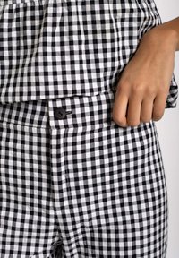 Tela de cuadros gingham en blanco y negro, con un corte relajado, cierre de botón en la cintura y un acabado suave y texturizado.