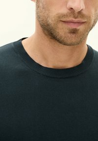 Dark green knit sweater with a round neck, featuring a ribbed collar. The fabric appears smooth with a subtle texture.