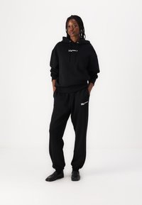 Black hoodie and sweatpants set, made from soft material. Hoodie features a front logo and adjustable drawstring; pants have side pockets.