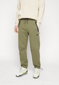 Oliwkowe dresy z elastycznym paskiem w talii i czarnym sznurkiem. Posiadają boczne kieszenie oraz małe czarne logo Nike na udzie.