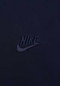 Tecido azul-marinho com uma superfície texturizada, apresentando um logótipo da Nike em preto bordado. Design simples e limpo, sem padrões ou detalhes adicionais.