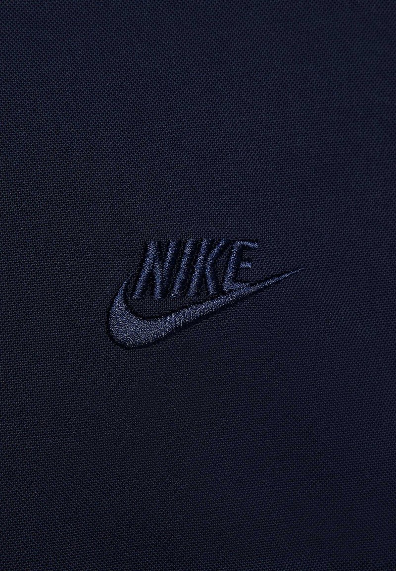 Tissu marine avec une surface texturée présentant un logo Nike noir brodé. Design simple et épuré sans motifs ou détails supplémentaires.