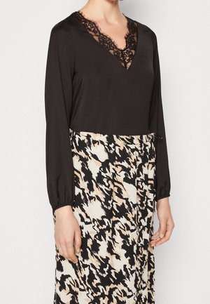 Blusa nera con scollatura a V in pizzo e maniche lunghe abbinata a una gonna a fantasia con tonalità di nero, crema e beige. Dettaglio con vita elastica.