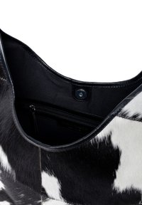 Svart och vit koshudsväska med en slät yta, med en dragkedjeficka och en svart foder. Rundad, öppen design.