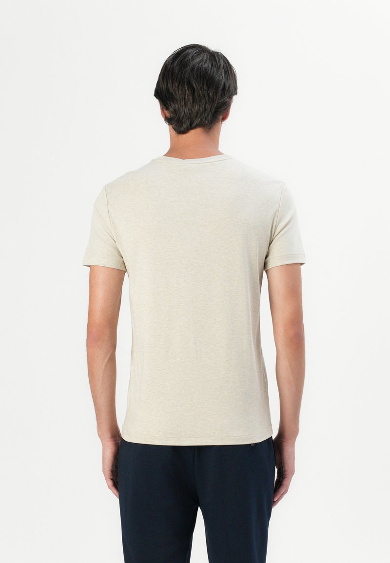 Camiseta de manga corta beige, diseño de cuello redondo, textura suave, detalles mínimos, silueta ajustada, exhibida en un modelo visto desde la espalda.