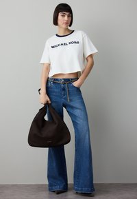 Witte cropped t-shirt met marineblauwe afwerking en "MICHAEL KORS" logo, gecombineerd met wijde blauwe spijkerbroek en een zwarte hobo-tas.