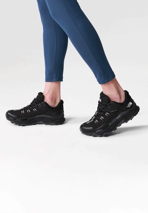 Zapatillas deportivas negras con superior de malla, un collar acolchado y cordones blancos en contraste. Suela de goma moldeada con diseño texturizado para mayor tracción.