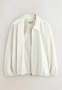 Bela lahka jakna s ovratnikom, sprednjo zadrgo, elastičnimi manšetami in spodnjim robom, obešena na enostavni svetli podlagi.