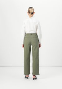 Pantaloni larghi verdi in tessuto morbido con tasche posteriori. Abbinati a una camicia bianca a maniche lunghe e scarpe nere con tacco.