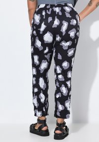 Schwarze Hose aus strukturiertem Stoff mit einem grauen und weißen abstrakten Muster. Elastischer Bund und Seitentaschen. Kombiniert mit schwarzen Sandalen.