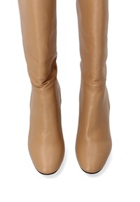 Beige Überknie-Stiefel aus glänzendem Leder, mit einem schlanken, taillierten Design, runder Schuhspitze und minimalen Nähdetails.