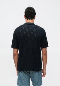 Navyblauw poloshirt met korte mouwen, voorzien van een gestructureerd diamantpatroon en gebreide stof, met een geribbelde kraag en manchetten.