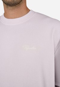 Light purple ribbed sweatshirt with a round neck and small white embroidered logo on the left chest. Soft texture and relaxed fit.