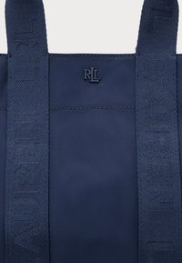 Sac cabas bleu marine avec deux larges anses embossées "LAUREN RALPH LAUREN" et un petit logo "RL" en relief entre les anses.