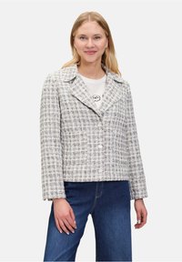 Textured, cropped jas in wit en grijs tweed. Voorzien van een gesneden kraag, knopenfront en lange mouwen. Gecombineerd met blauwe jeans.