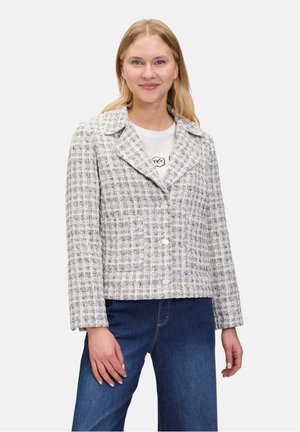 Veste texturée et raccourcie en tweed blanc et gris. Présente un col cranté, une fermeture à boutons et des manches longues. Associée à un jean bleu.