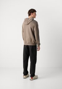 Felpa marrone con cappuccio regolabile, abbinata a pantaloni in denim scuri dal taglio largo. Presenta polsini a costine e un design semplice.