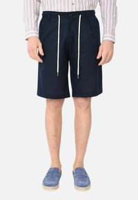 Pantaloni corti blu navy in un tessuto leggero, con vita regolabile tramite cordino e tasche laterali. Abbinati a scarpe slip-on azzurro chiaro.