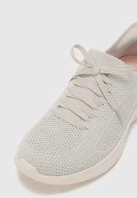 Light gray textile sneaker featuring a breathable mesh upper, flat laces, padded collar, and a textured sole. Minimalist design and flexibility.